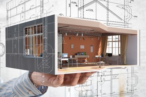 Hand hält ein Modell eines modernen Raums mit Möbeln und Architekturzeichnungen im Hintergrund.